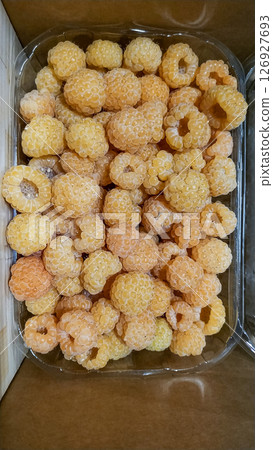 Golden raspberries filling a plastic container on a table Golden raspberries filling a plastic container on a table 126927693