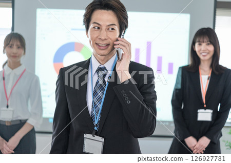 一名西裝革履的男子在會議室的螢幕前用智慧型手機交談 126927781