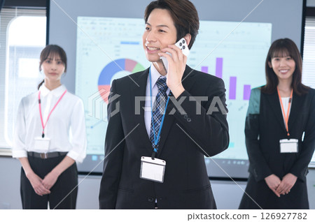 一名西裝革履的男子在會議室的螢幕前用智慧型手機交談 一名西裝革履的男子在會議室的螢幕前用智慧型手機交談 126927782