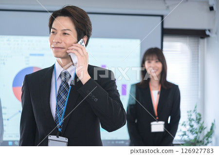 一名西裝革履的男子在會議室的螢幕前用智慧型手機交談 126927783