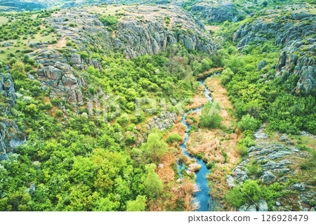 Aerial drone view of a stream running through a canyon in the mountains in the middle of a sunny summer day. 126928479