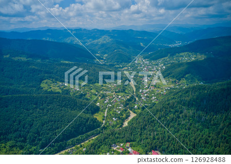 Aerial drone view footage of a city surrounded by green mountains. 126928488