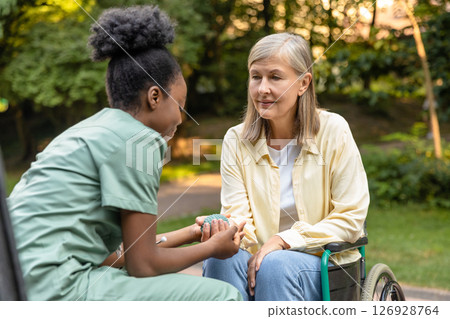 Nurse working with a patient in the park and helping her to do rehabilitation exercising 126928764