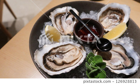 close up of four pieces of fresh raw oysters with vinegar and lemon slice on ice in a big plate with copy space 126928813