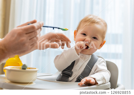 Father and a cute little baby boy having breakfast in the kitchen Father and a cute little baby boy having breakfast in the kitchen 126928855