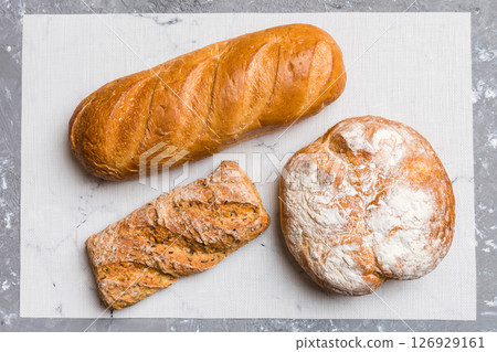 Assortment of freshly baked bread with napkin on rustic table top view. Healthy unleavened bread. French bread Assortment of freshly baked bread with napkin on rustic table top view. Healthy unleavened bread. French bread 126929161
