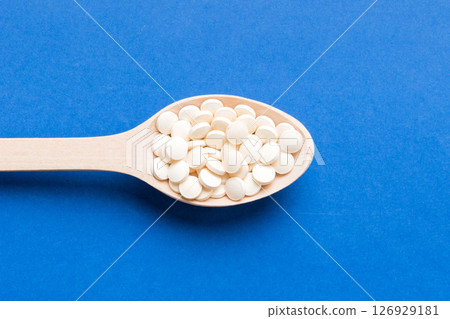 Heap of white pills on colored background. Tablets scattered on a table. Pile of red soft gelatin capsule. Vitamins and dietary supplements concept Heap of white pills on colored background. Tablets scattered on a table. Pile of red soft gelatin capsule. Vitamins and dietary supplements concept 126929181