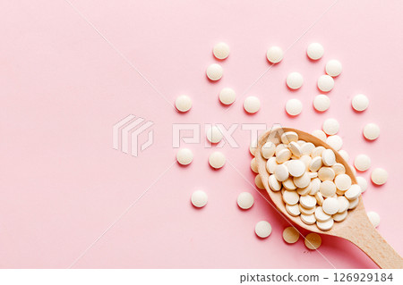 Heap of white pills on colored background. Tablets scattered on a table. Pile of red soft gelatin capsule. Vitamins and dietary supplements concept Heap of white pills on colored background. Tablets scattered on a table. Pile of red soft gelatin capsule. Vitamins and dietary supplements concept 126929184
