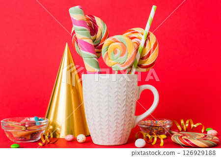 Colorful candies in cup on table on light background background. Large swirled lollipops. Creative concept of a jar full of delicious sweets from the candy store Colorful candies in cup on table on light background background. Large swirled lollipops. Creative concept of a jar full of delicious sweets from the candy store 126929188