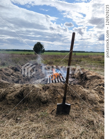 shovel in the sand on a background of a campfire and wooden bars. bonfire and shovel 126929235