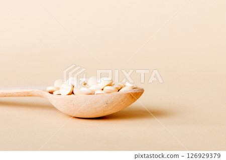 Heap of white pills on colored background. Tablets scattered on a table. Pile of red soft gelatin capsule. Vitamins and dietary supplements concept 126929379