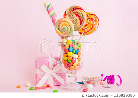 Colorful candies in cup on table on light background background. Large swirled lollipops. Creative concept of a jar full of delicious sweets from the candy store Colorful candies in cup on table on light background background. Large swirled lollipops. Creative concept of a jar full of delicious sweets from the candy store 126929390