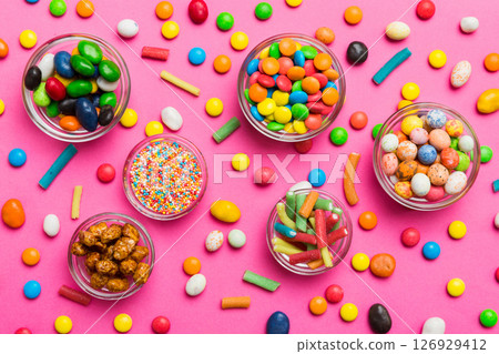 different colored round candy in bowl and jars. Top view of large variety sweets and candies with copy space different colored round candy in bowl and jars. Top view of large variety sweets and candies with copy space 126929412