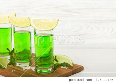Sweet refreshing mint liqueur, with ice and mint leaves on table background, Shots with lime slice and mint flat lay Sweet refreshing mint liqueur, with ice and mint leaves on table background, Shots with lime slice and mint flat lay 126929426