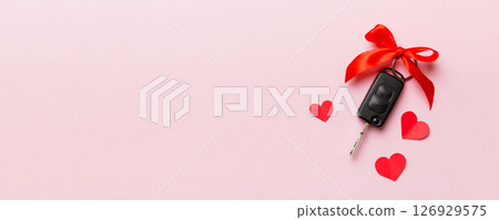 Car key with a red bow and a heart on Colored table. Giving present or gift for valentine day or christmas, Top view with copy space 126929575