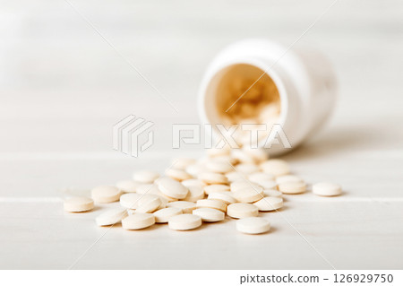 Medicine bottle and white pills spilled on a light background. Medicines and prescription pills flat lay background. White medical pills and tablets spilling out of a drug bottle Medicine bottle and white pills spilled on a light background. Medicines and prescription pills flat lay background. White medical pills and tablets spilling out of a drug bottle 126929750
