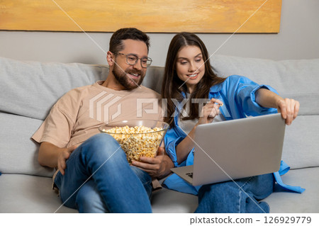 Woman and her boyfriend watching movie on laptop while eating junk popcorn Woman and her boyfriend watching movie on laptop while eating junk popcorn 126929779