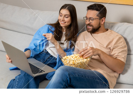 Woman and her boyfriend watching movie on laptop while eating junk popcorn Woman and her boyfriend watching movie on laptop while eating junk popcorn 126929786