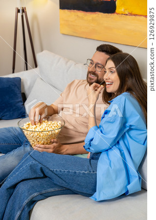 Couple in casual clothes sitting on couch with popcorn at home 126929875