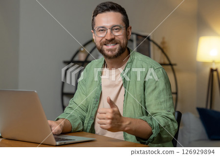 Man sitting at desk working on laptop showing thumb up like gesture Man sitting at desk working on laptop showing thumb up like gesture 126929894