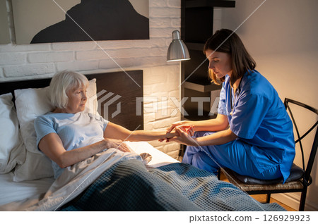 Doctor checking pulse of an elderly patient and looking focused Doctor checking pulse of an elderly patient and looking focused 126929923