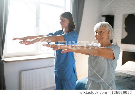 Elderly lady exercising with an instructor and looking involved 126929933