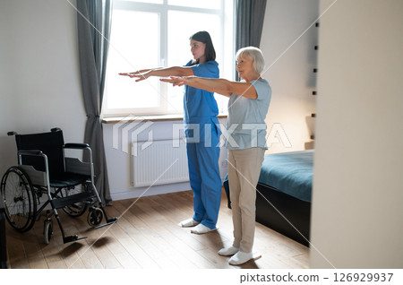 Elderly lady exercising with an instructor and looking involved Elderly lady exercising with an instructor and looking involved 126929937