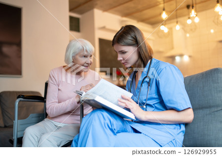 Female care assistant reading a book to a elderly lady and both looking enjoyed 126929955