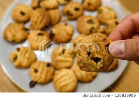 close up of homemade freshly baked raisin cookies flat lay on the plate with copy space with a finger holding one piece of cookie close up of homemade freshly baked raisin cookies flat lay on the plate with copy space with a finger holding one piece of cookie 126929999