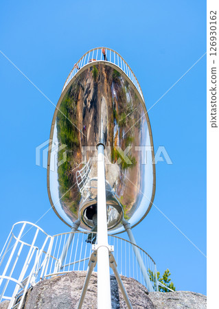 Visitors enjoy breathtaking views from the Sipka lookout platform in the Jizera Mountains, Czechia, surrounded by lush greenery and a clear blue sky on a sunny day. 126930162