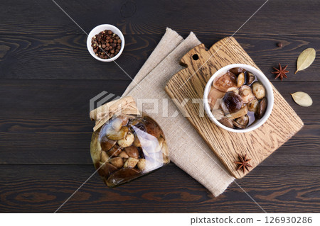 Pickled mushrooms in a glass jar and bowl on dark rustic wooden background. 126930286