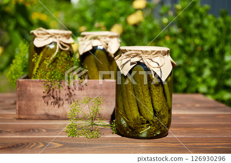 Jars of pickled cucumbers on a wooden table in the garden on a sunny summer day Jars of pickled cucumbers on a wooden table in the garden on a sunny summer day 126930296