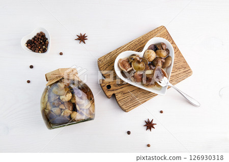 Pickled mushrooms in a glass jar and bowl on white wooden background. Pickled mushrooms in a glass jar and bowl on white wooden background. 126930318