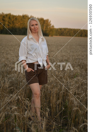 Woman sitting in a golden wheat field during sunset, capturing a serene moment of connection with nature under warm light Woman sitting in a golden wheat field during sunset, capturing a serene moment of connection with nature under warm light 126930560