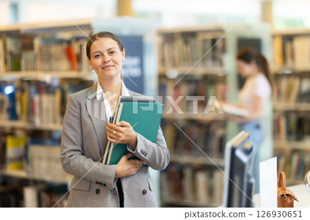 Young female student stands in library with stack of books 126930651