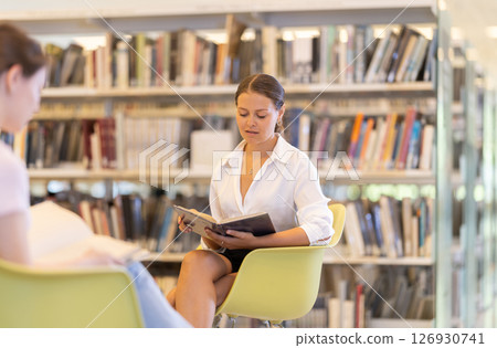Female sitting on a chair in the library against the background of students Female sitting on a chair in the library against the background of students 126930741