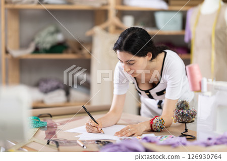 Female fashion designer sketching new clothing ideas in sewing studio 126930764