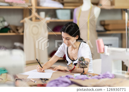 Female fashion designer sketching new clothing ideas in sewing studio 126930771