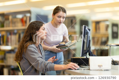 Two female students near the monitor in the library Two female students near the monitor in the library 126930790