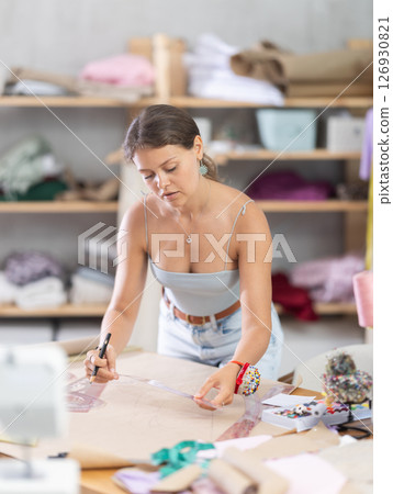 Female dressmaker sketching clothing pattern with curve ruler in workshop Female dressmaker sketching clothing pattern with curve ruler in workshop 126930821