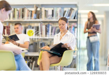 Female student sitting with book in library on shelving background 126930833
