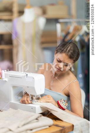 Young seamstress sewing on a machine in a workshop 126930834