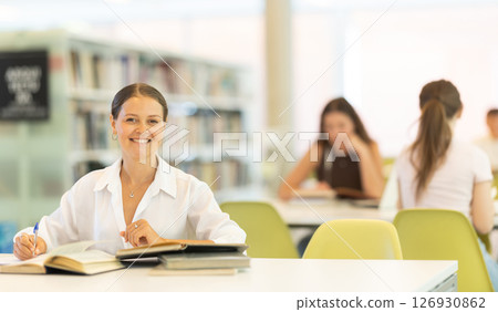 Female student reading book and taking notes in library 126930862