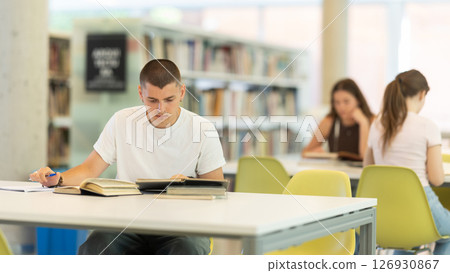 guy is sitting at the table, reading a book and taking notes 126930867