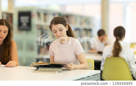 Female student sitting at table and writing Female student sitting at table and writing 126930895
