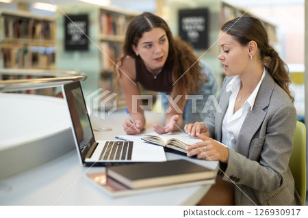 female student works at a notebook, and a fellow student helps her female student works at a notebook, and a fellow student helps her 126930917