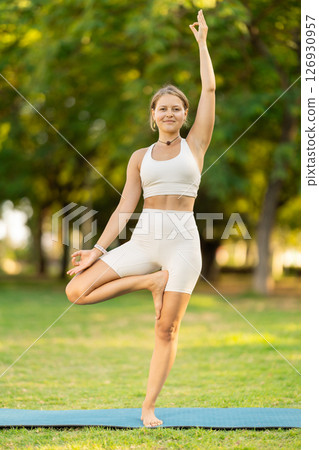 Girl in park on green grass of lawn performs Ardha Baddha Padma Vrikshasana 126930957