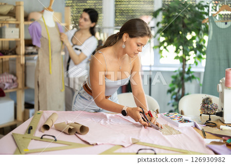 Female tailor cutting fabric while teammate working with mannequin Female tailor cutting fabric while teammate working with mannequin 126930982