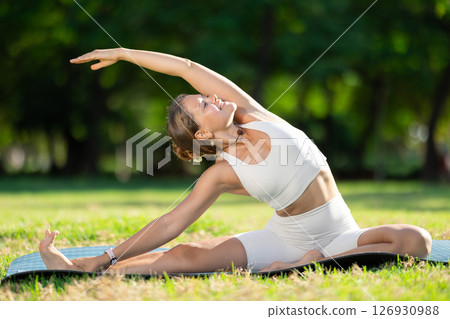 Girl in park on green grass of lawn performs Parivritta Janu Shirshasana 126930988