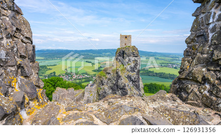Trosky Castle Ruins stand majestically on rocky peaks in Bohemian Paradise, Czechia. Visitors admire the stunning landscape framed by verdant fields and distant hills on a clear day. 126931356